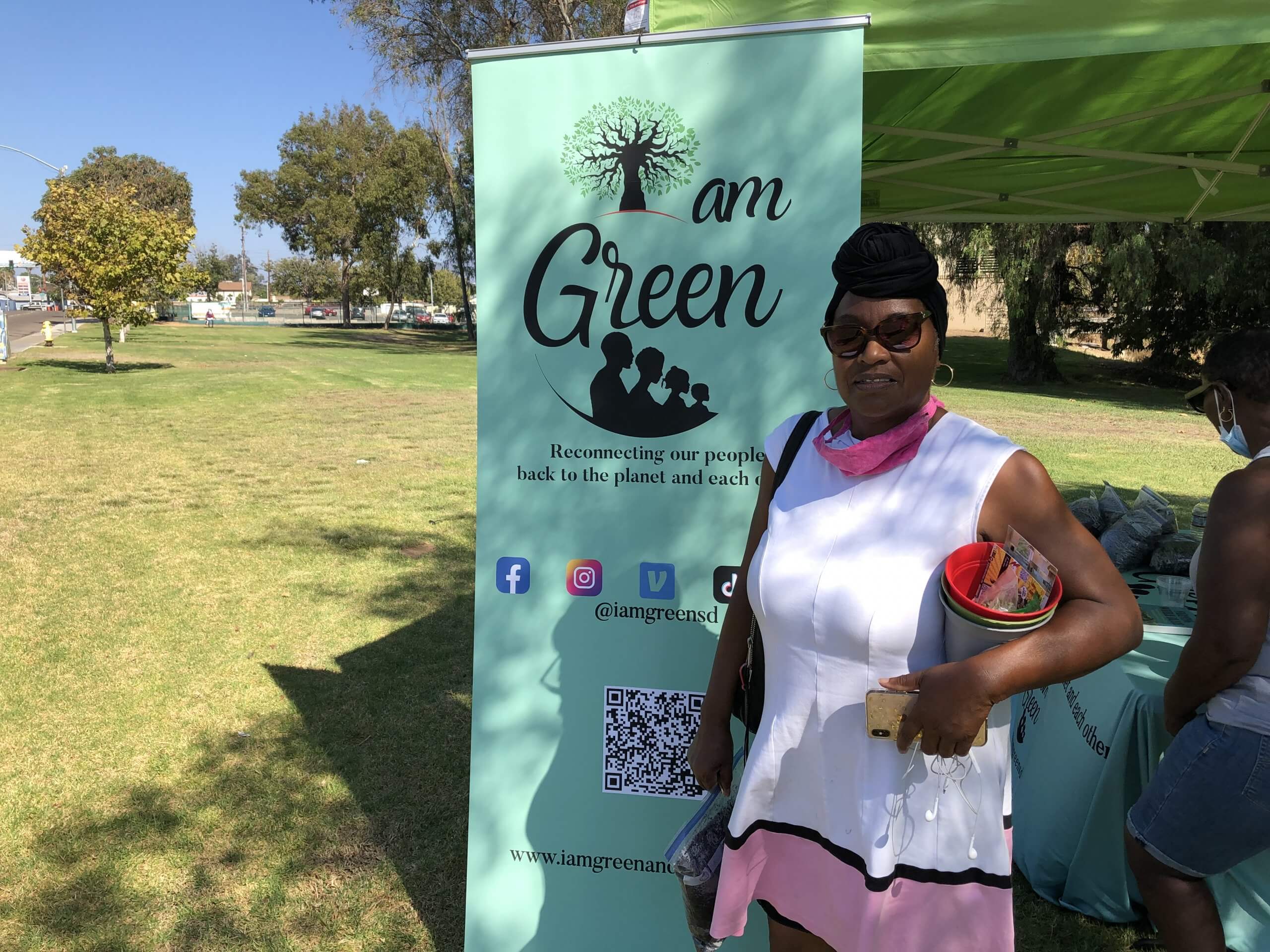 A person standing next to an "I am Green" sign outside on a sunny day