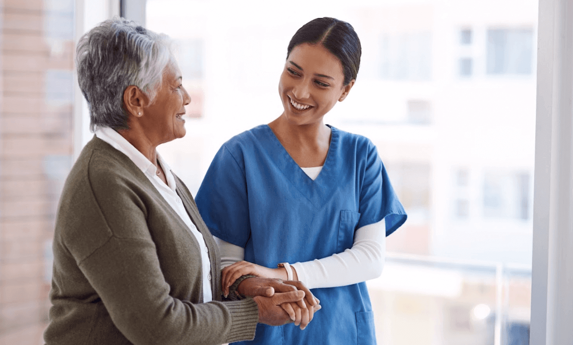 A nurse is holding the hands of an older person as they smile at each other and walk forward