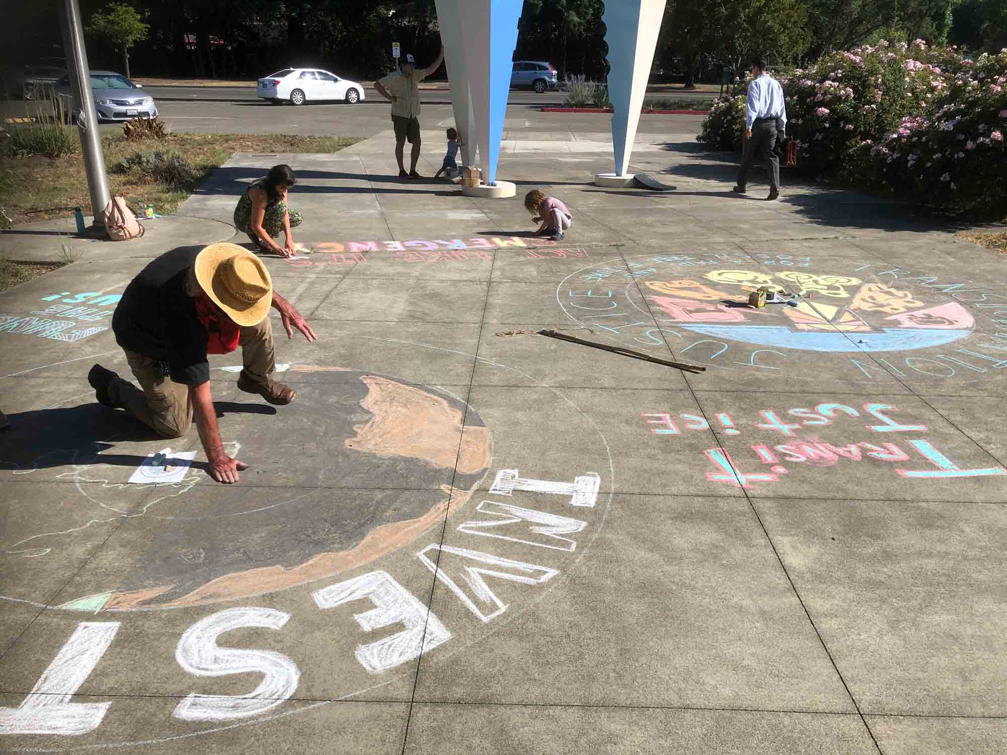 three people drawing messages with chalk on a sidewalk