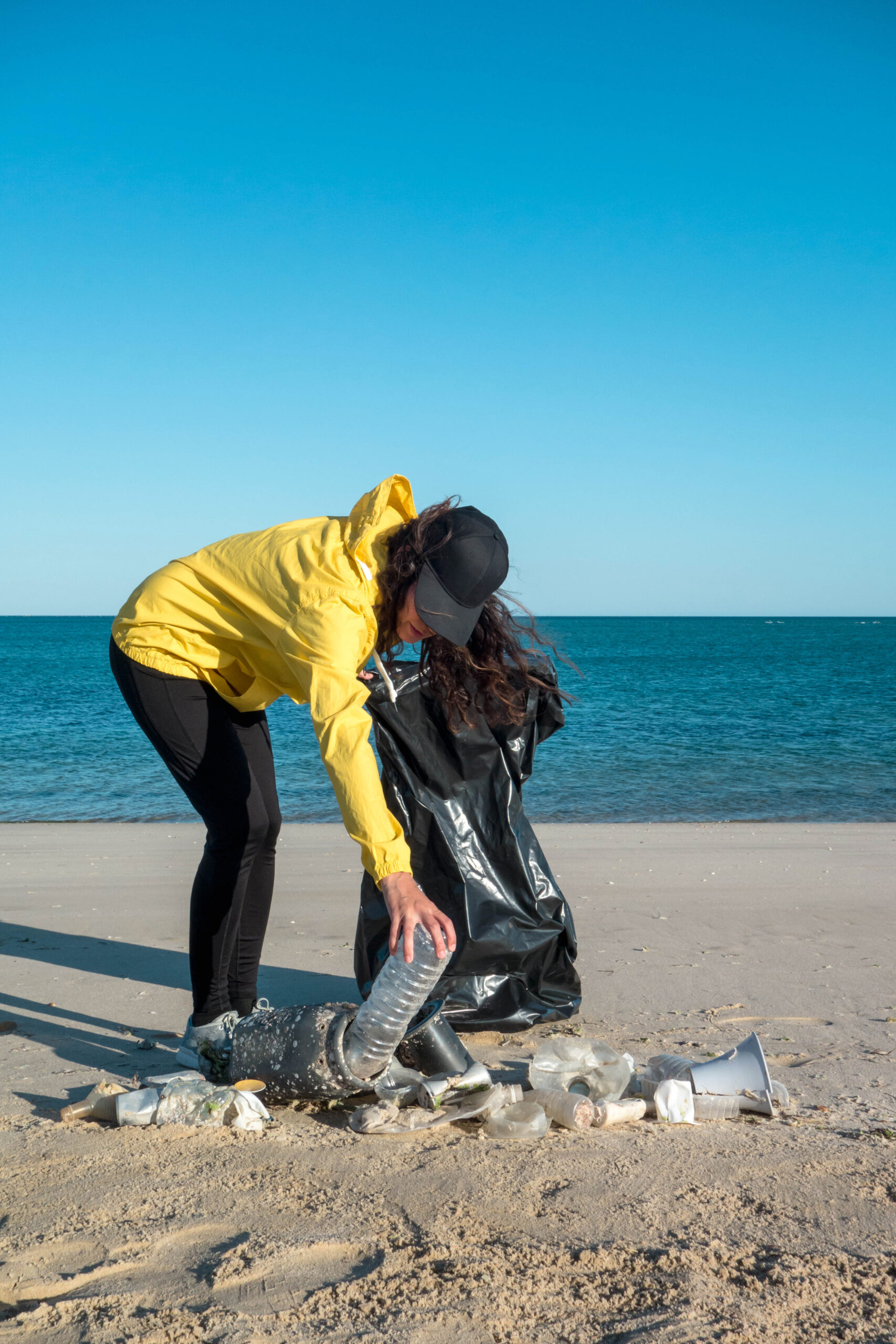 Adult in yellow jacket picking up trash on the beach